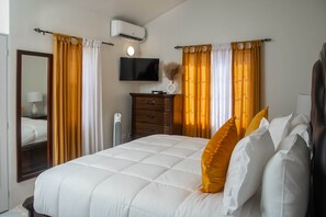 A hotel room with a bed, a dresser, a television, and an air conditioning unit. - Luxury Overlooking Puerto Seco Beach @ Camelot (Discovery Bay)