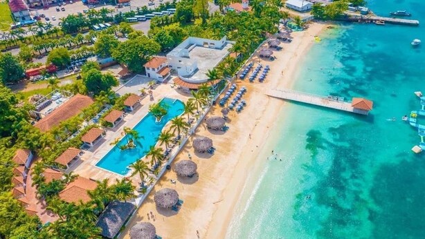 An aerial view of a resort with a swimming pool, beach, and pier.