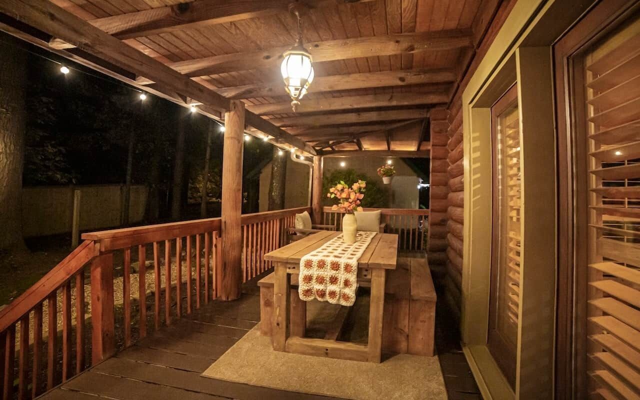 A wooden deck with a table and chairs, a hanging light fixture, and a view of the surrounding area.