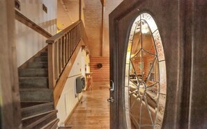 A wooden staircase leading to a log cabin interior with a large, arched door.