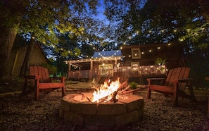 A rustic cabin with a fire pit, wooden deck, and string lights.