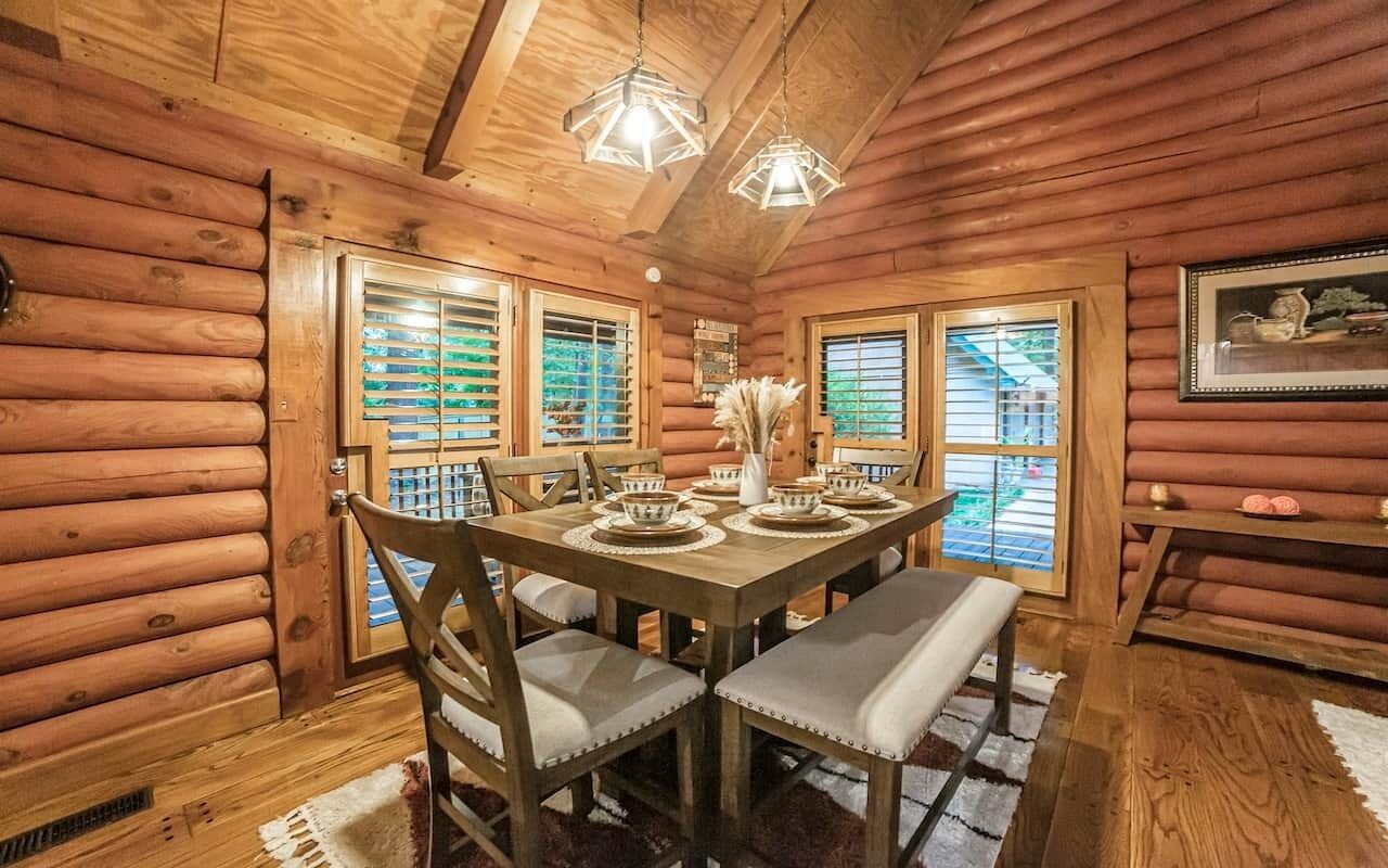 Interior de una cabaña de madera con una mesa de comedor, sillas y una araña.