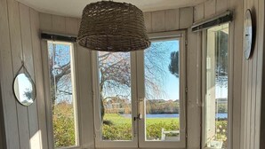Een ronde tafel met een tafelkleed met patroon, vier zwarte stoelen, een geweven hanglamp en uitzicht op een meer door grote ramen.