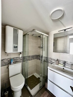 Un bagno con doccia vetro, un water, un lavandino con specchio e un armadietto bianco.