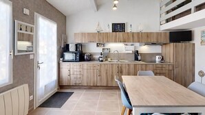 A compact kitchen with wooden cabinets, a microwave, a stove, and a dining area with a table and chairs. - L'escapade du Maupas - house 5 min from the beach (La Tranche-sur-Mer)