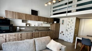 A modern kitchen with a built-in oven, a dining area with a table and chairs, and a grey sofa with pillows. - L'escapade du Maupas - house 5 min from the beach (La Tranche-sur-Mer)