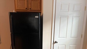 A kitchen with a black refrigerator, wooden cabinets, a white door, and beige tiled flooring.