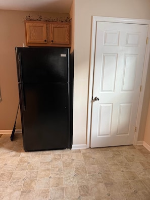 Una cocina con un refrigerador negro, armarios de madera, una puerta blanca y piso de baldosas color beige.