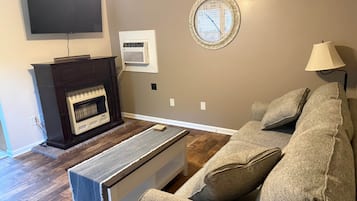A living room with a fireplace, a flat-screen TV, a clock, and a sofa.