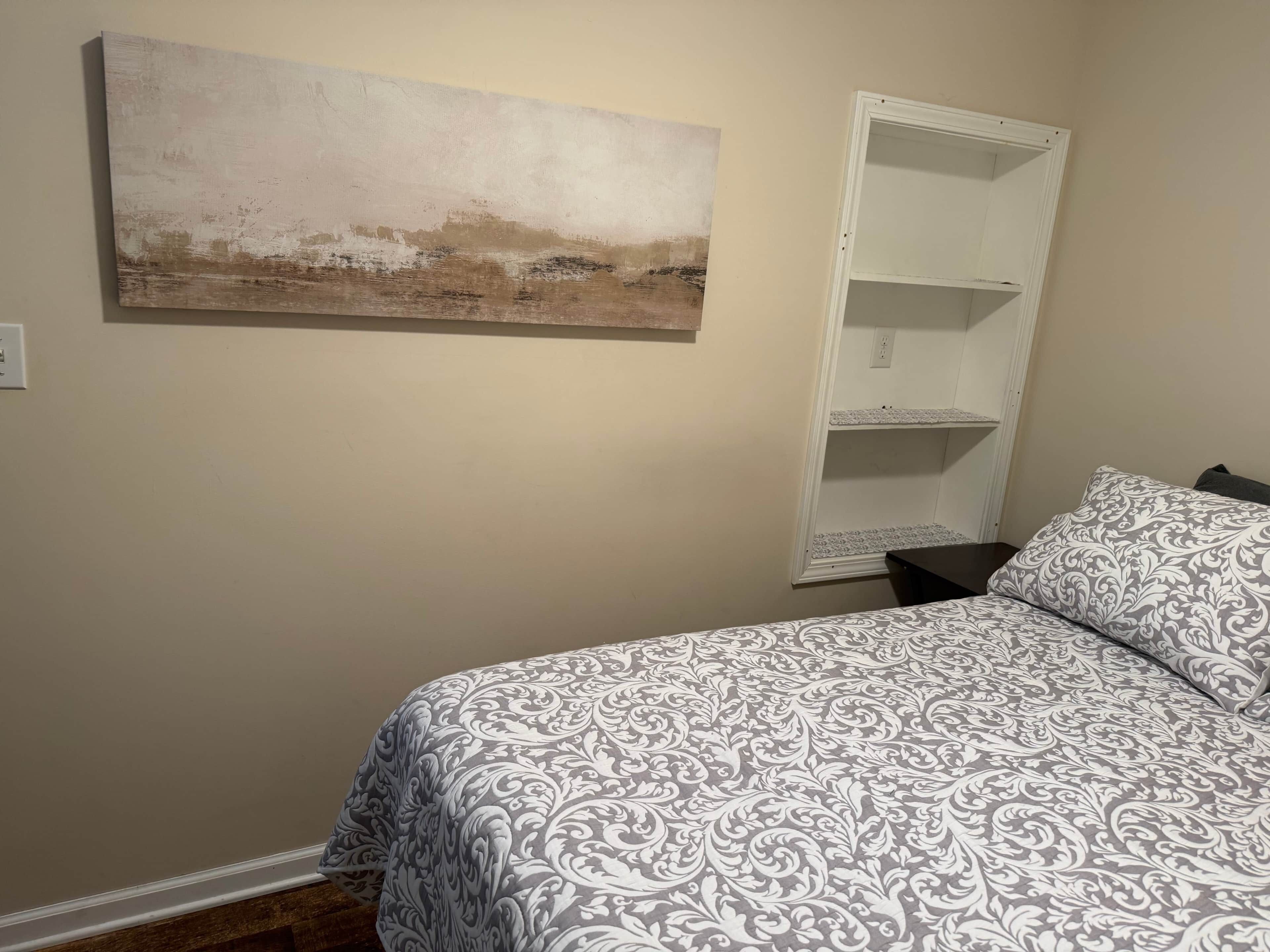 Une chambre avec un lit, une étagère blanche et un tableau accroché au mur.