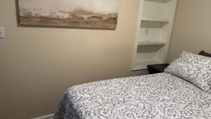A bedroom with a bed, a white shelving unit, and a painting on the wall.