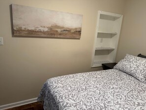 Un dormitorio con cama, una estantería blanca y un cuadro en la pared.