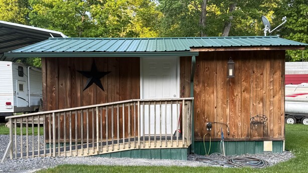 Una cabaña de madera con techo de metal, decoración de estrella, un pequeño porche y una antena parabólica.