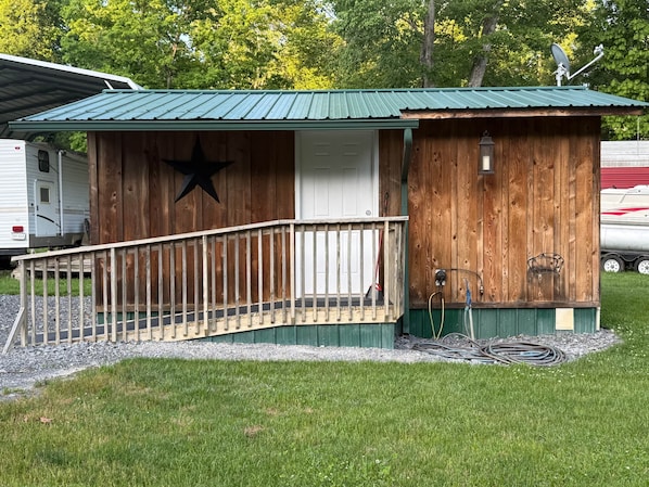A wooden cabin with a metal roof, a star decoration, a small porch, and a satellite dish.