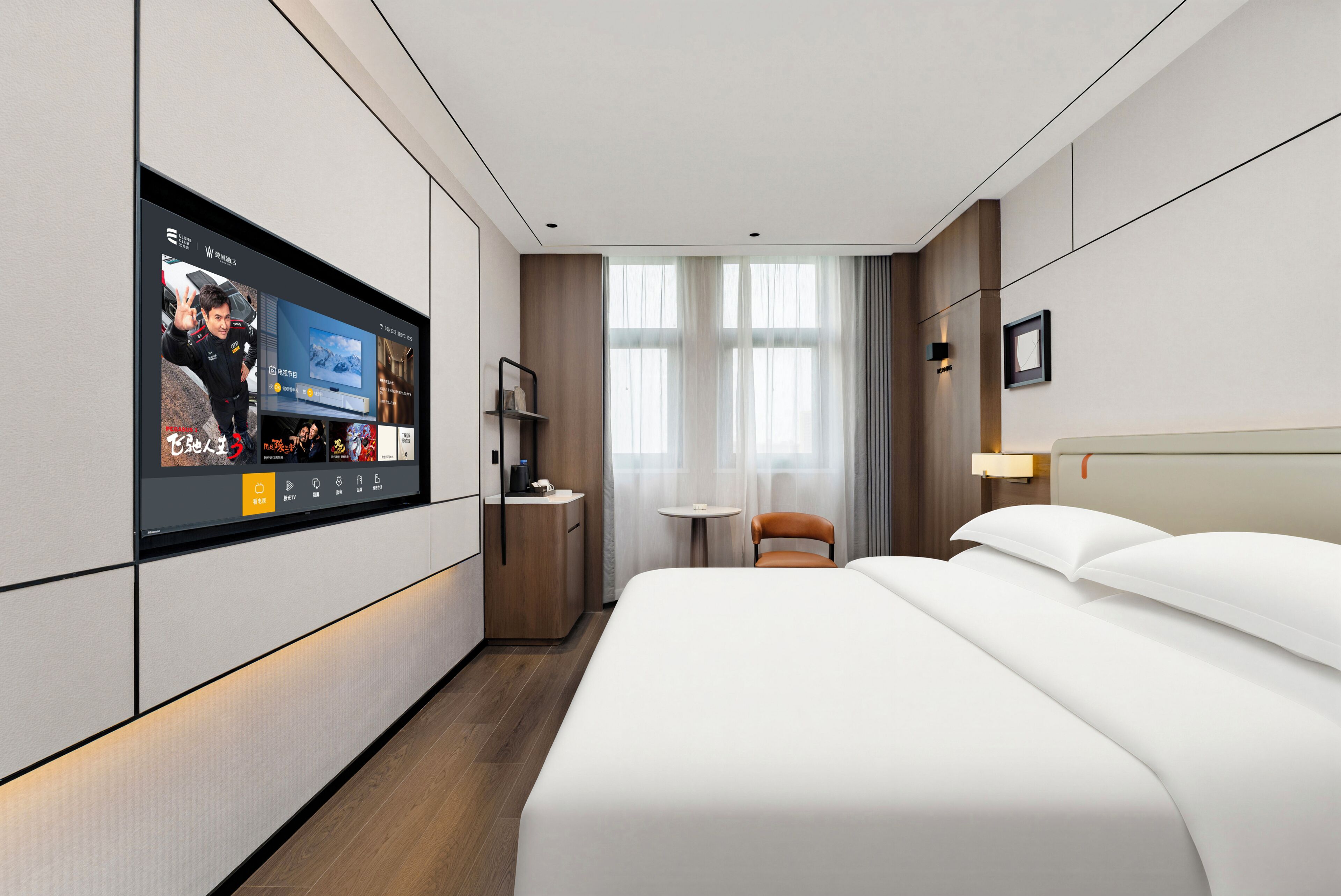 Ein Hotelzimmer mit einem großen Flachbildfernseher an der Wand, einem Bett mit weißer Bettwäsche, einem kleinen runden Tisch und einem Sessel.