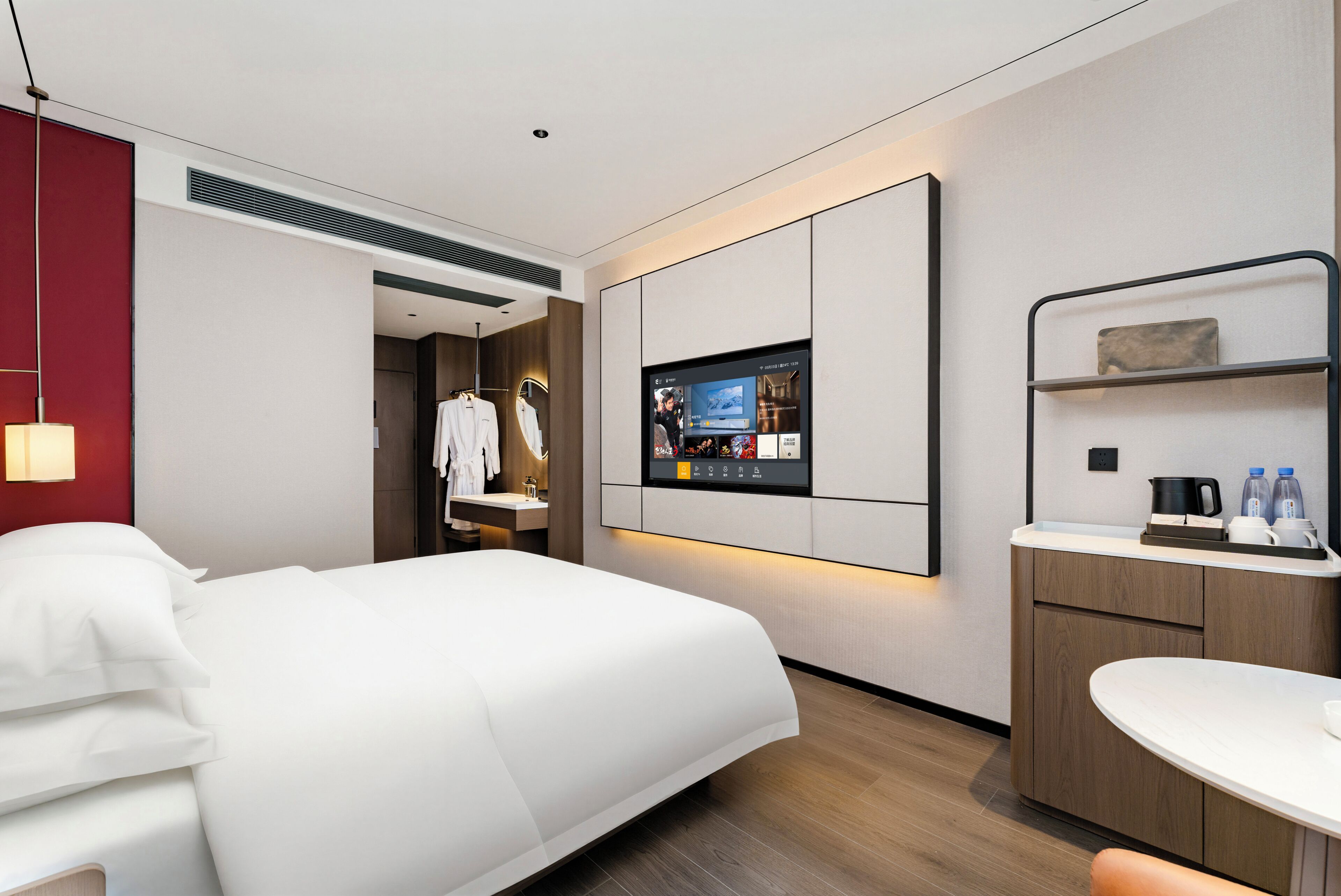Una habitación de hotel moderna con cama, televisor montado en la pared, una pequeña cocina y una pared de acento roja.