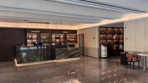 A modern hotel lobby with a marble reception desk, a seating area with a table and chairs, and a bookshelf filled with decorative items. - Morin Hotel (Zhengzhou)