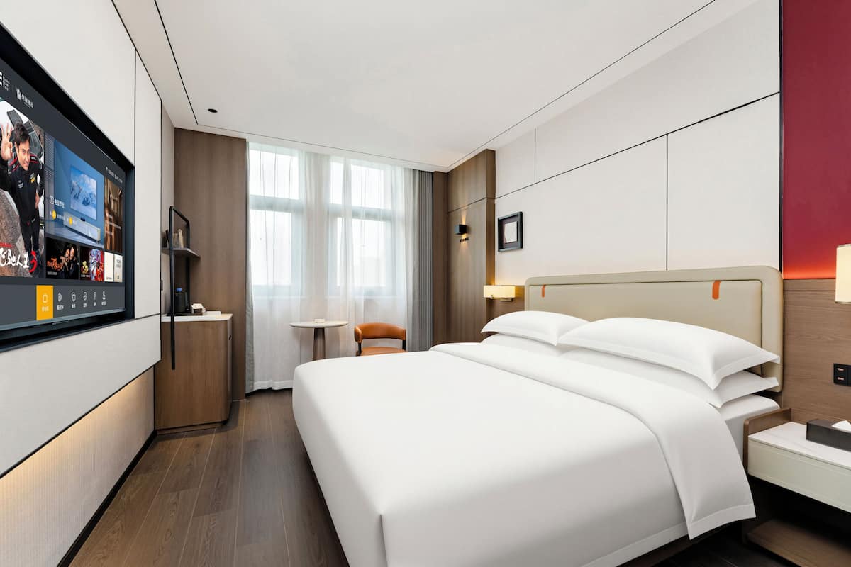 A hotel room with a large bed, a TV, a desk, and a chair.