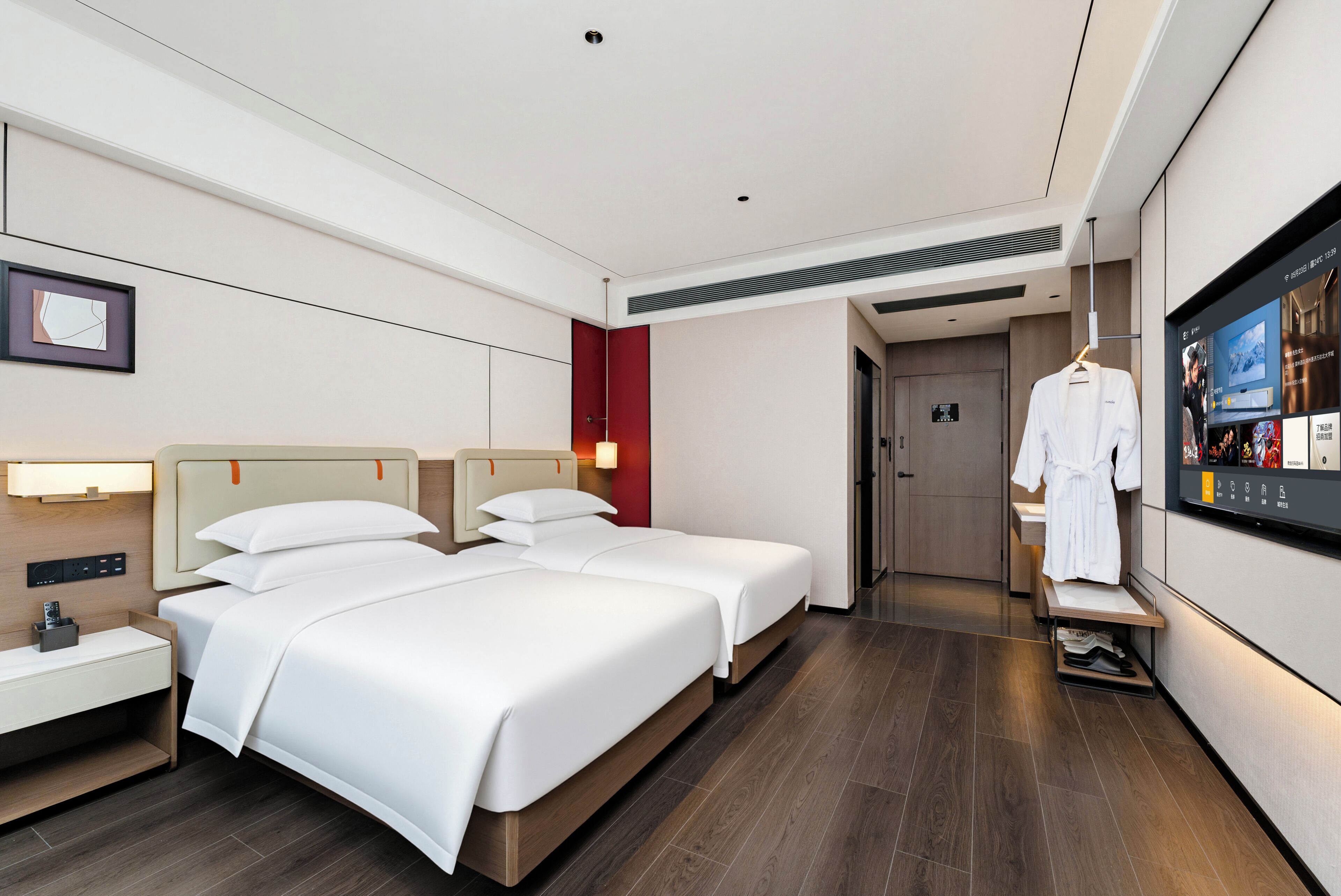 A hotel room with two beds, a TV, a robe rack, and a small desk with a lamp.