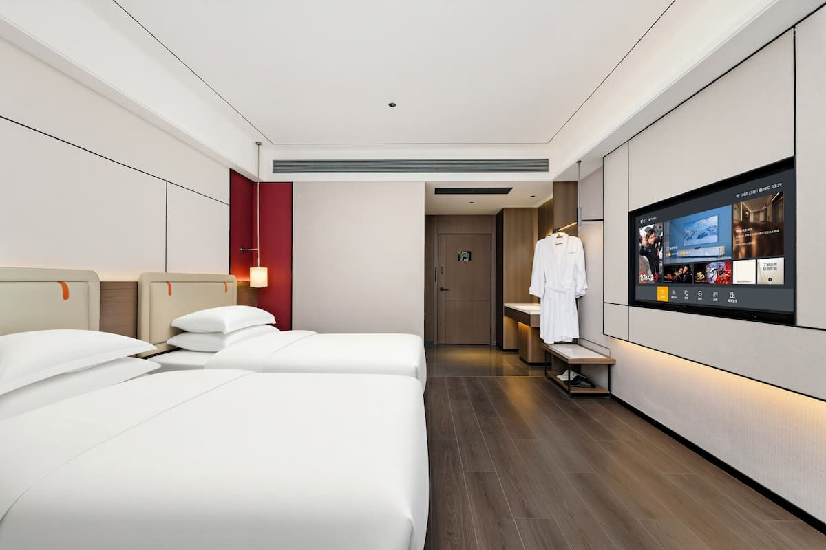 A hotel room with two beds, a TV, a mirror, and a red accent wall.