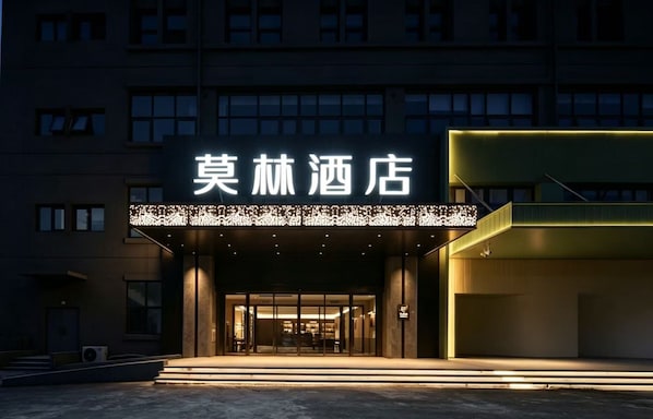 A hotel entrance with a modern facade, illuminated signage, and a visible entrance.