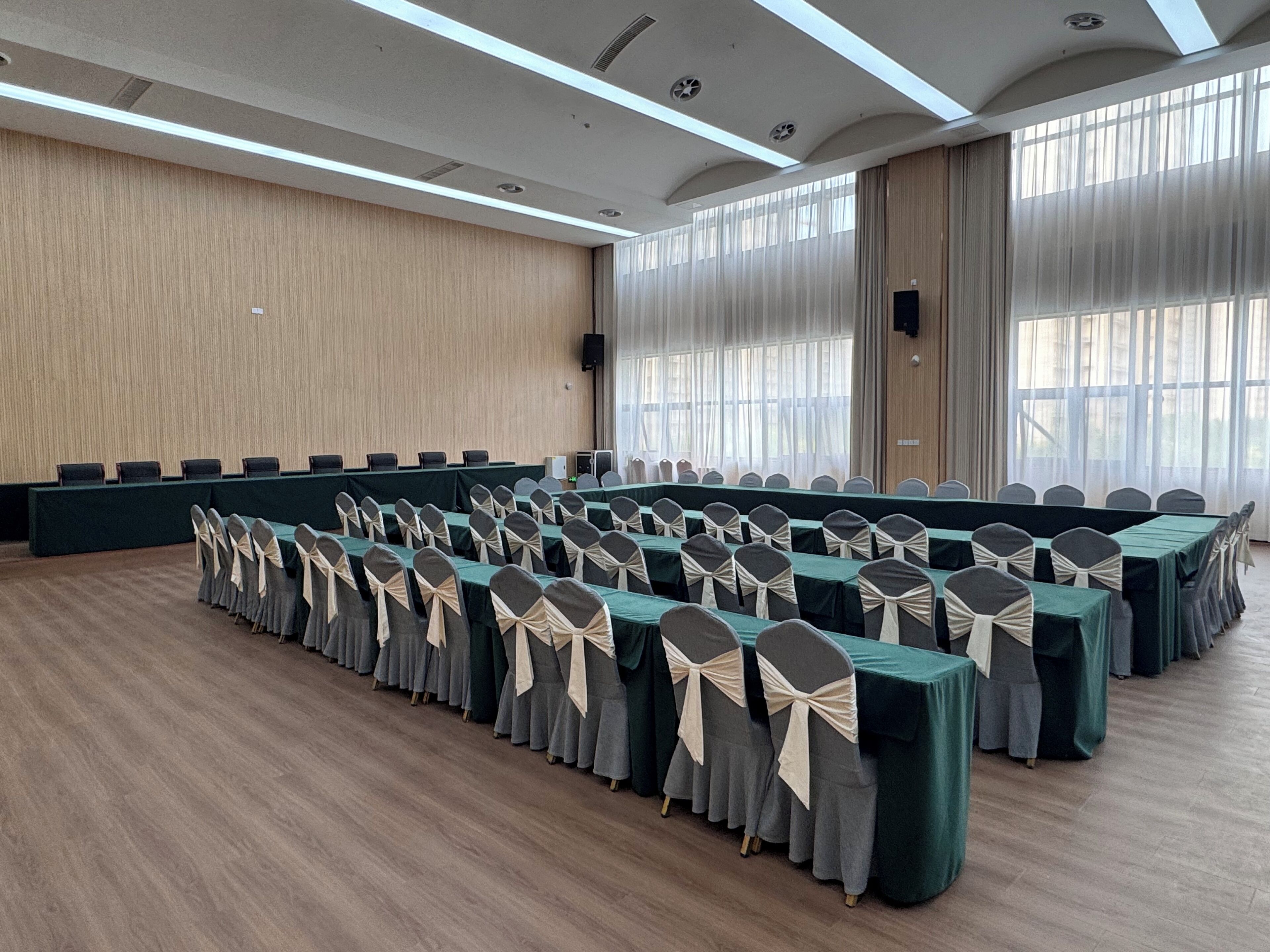 A conference room with rows of tables and chairs, large windows, and a wooden wall.