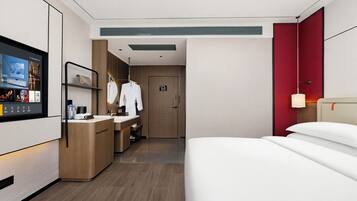 Una habitación de hotel moderna con cama, televisión, escritorio con computadora, mini refrigerador y baño con ducha e inodoro.