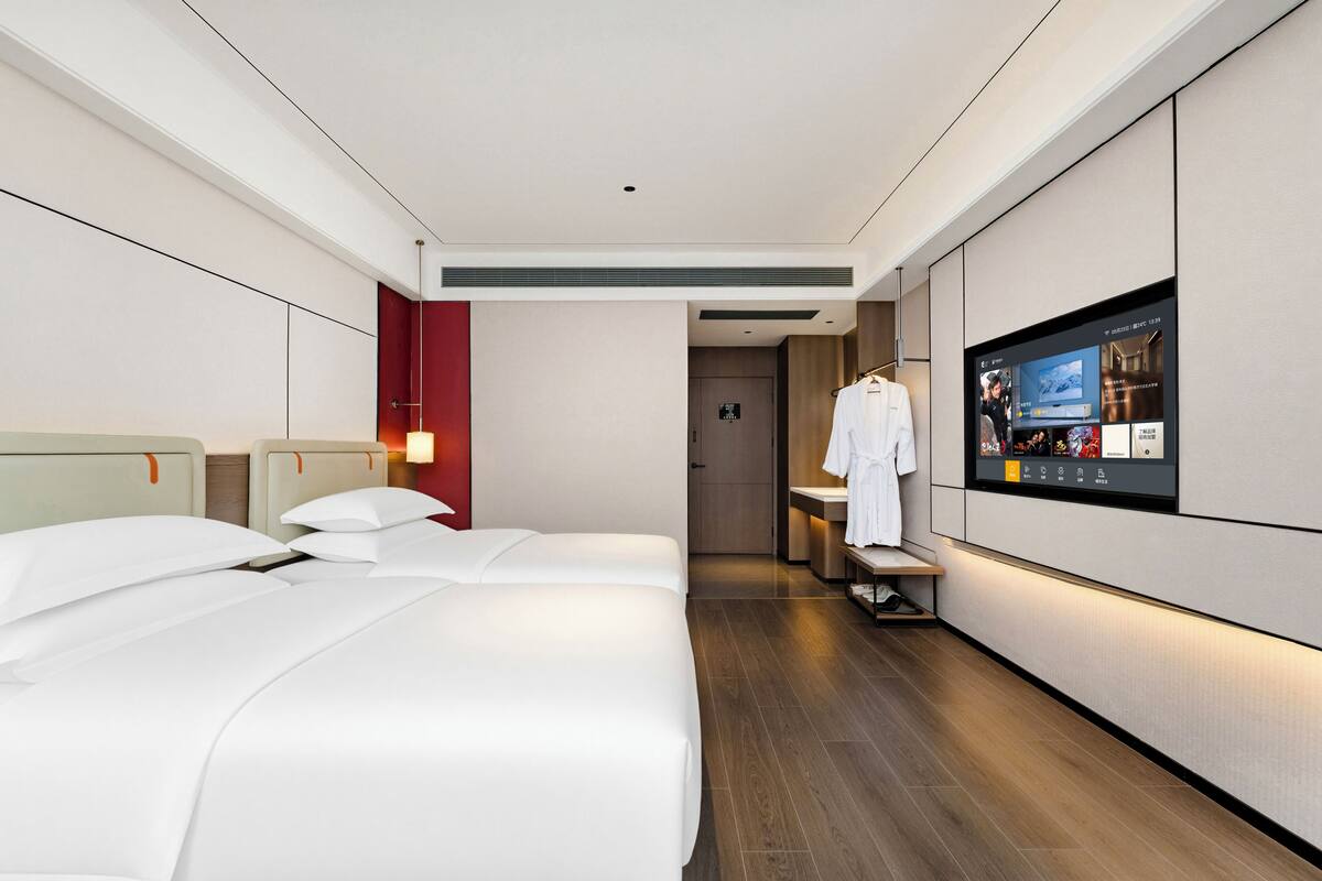 A hotel room with two beds, a TV, a robe rack, and a bathroom door.