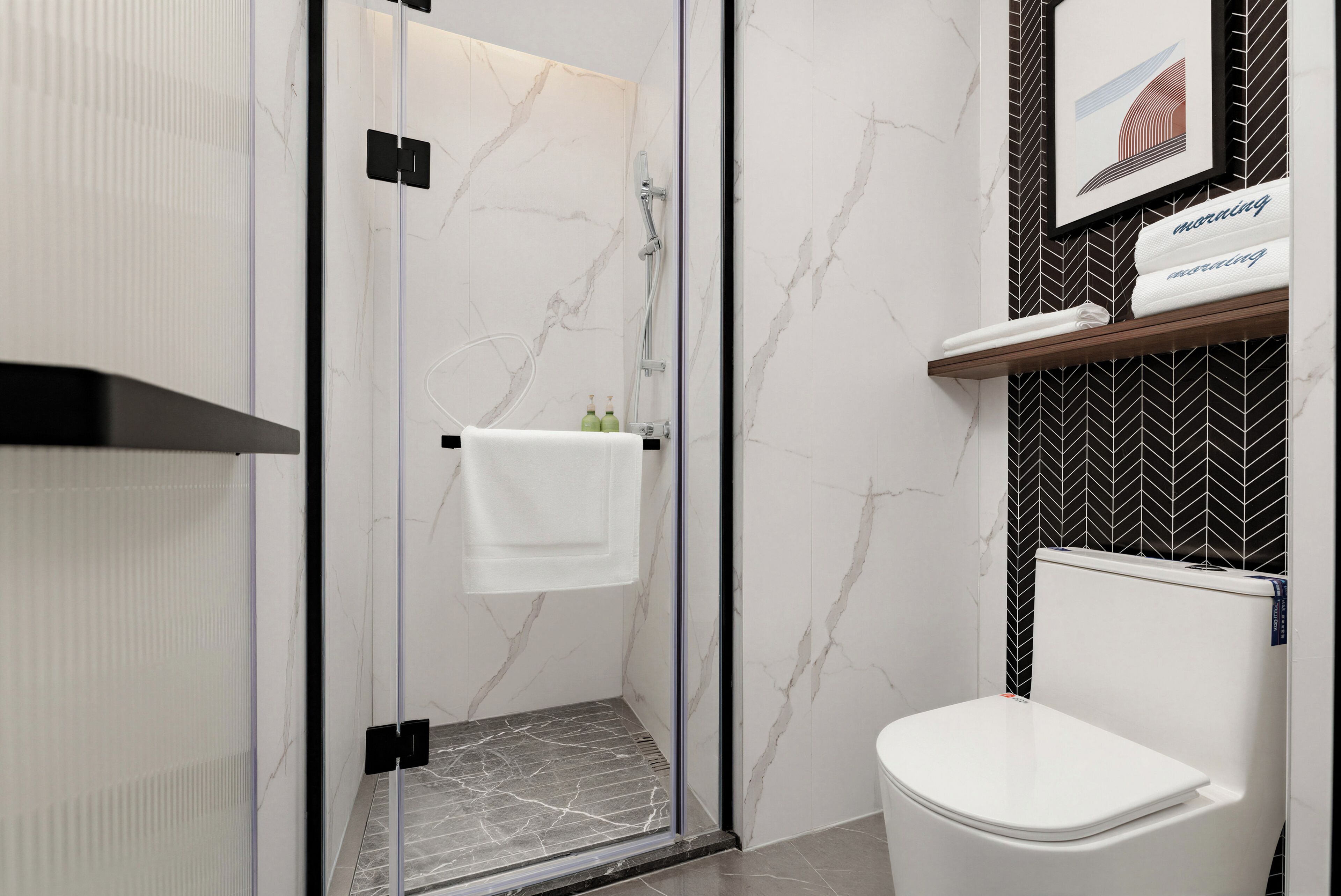 Un baño moderno con cabina de ducha de vidrio, un inodoro blanco y un perchero con una toalla blanca.