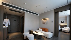 A modern hotel room with a sofa, ottomans, a coffee table, a robe rack, and a painting on the wall. - Morin Hotel (Zhengzhou)