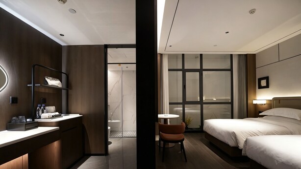 A modern hotel room with a wooden desk, a chair, a bed, and a small table. - Morin Hotel (Zhengzhou)
