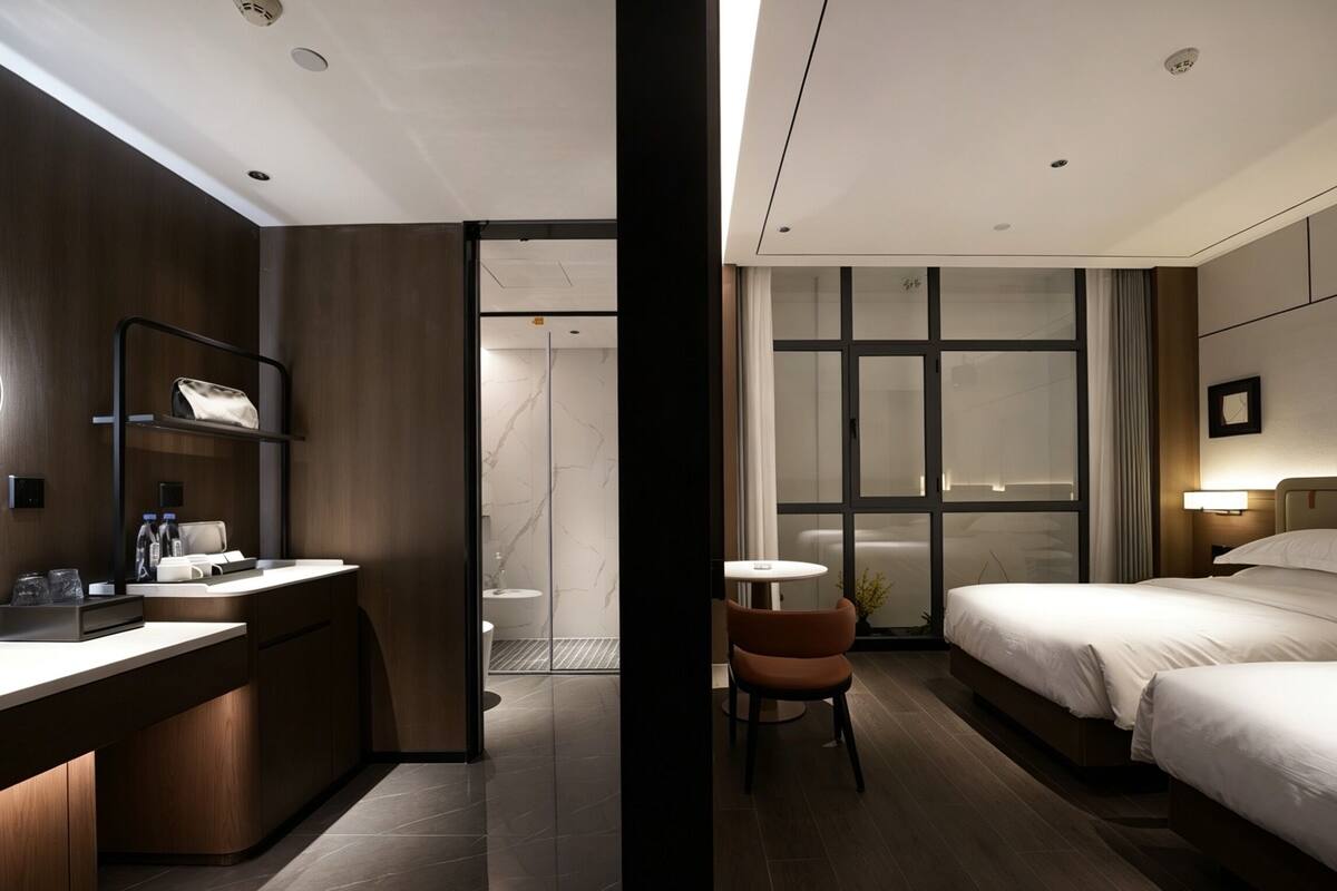 A modern hotel room with a wooden desk, a chair, a bed, and a small table.
