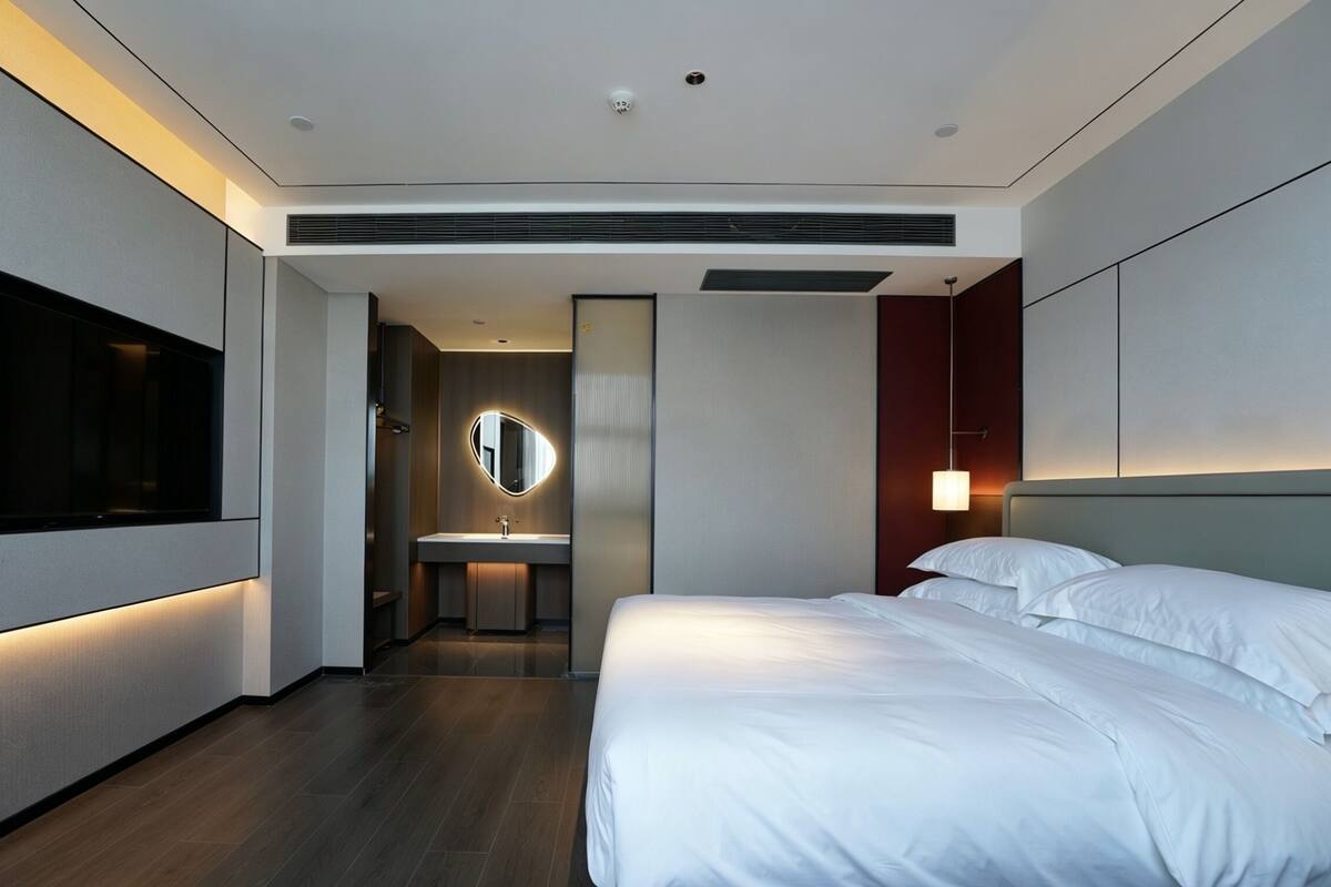 A modern hotel room with a large bed, a TV, a bathroom, and a view of the city.