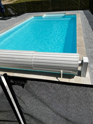 Une piscine à l’eau d’un bleu limpide, une chaise longue au bord de la piscine et un dispositif de couverture pour la piscine.