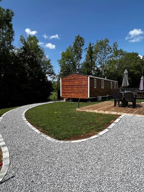 Une cabane moderne en bois, dotée d’un patio et entourée d’un chemin de gravier et de verdure.