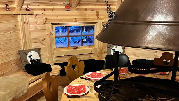 Un interior de madera acogedor con una mesa de comedor para cuatro, una chimenea y una ventana con vistas nevadas.