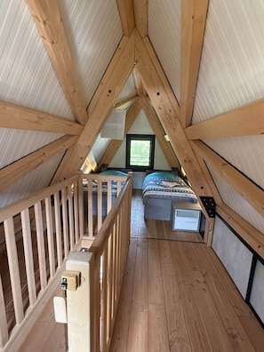 Ein schräg zulaufendes Schlafzimmer im Dachgeschoss mit Holzbalken, einem Fenster, einem Etagenbett und einem Hollgitter.