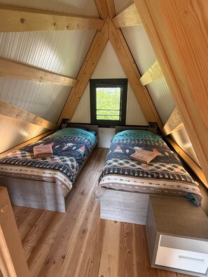 Quarto de sótão pequeno com duas camas, uma janela e vigas de madeira.