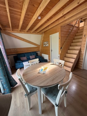 Une pièce chaleureuse avec un plafond en bois, une table ronde entourée de chaises, un canapé et un escalier.