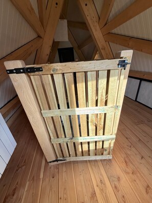 En träport med metallgångjärn och ett lås, placerad i ett rum med synliga träbjälkar och ett sluttande tak.