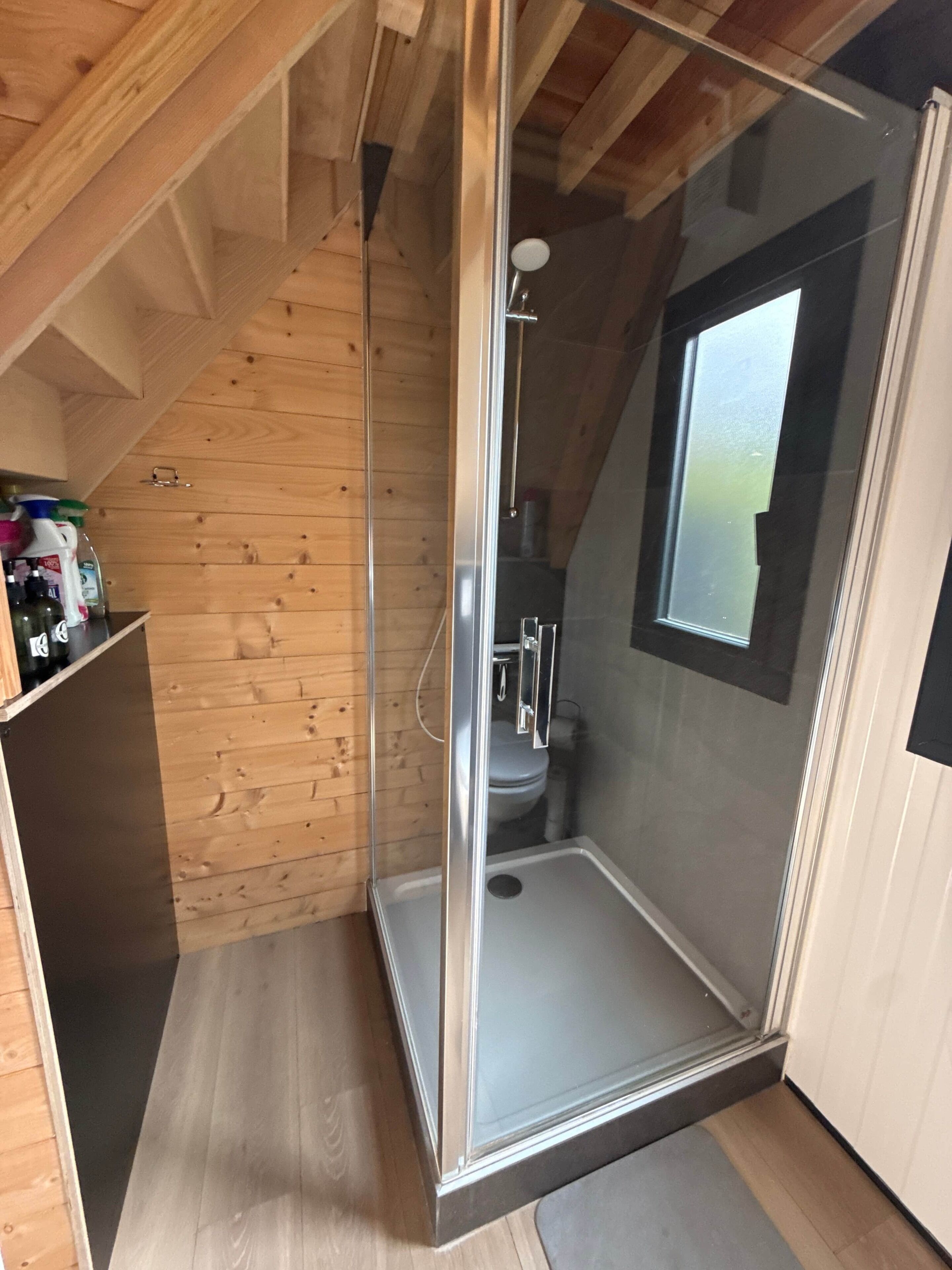 Een douchekamer met glazen wanden, een houten plafond en een raam.