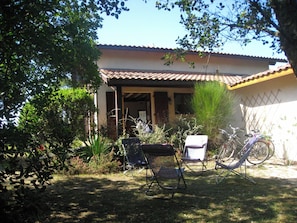 A house with a tiled roof, a covered porch, and a garden with chairs and bicycles. - Charming, quiet family home for golf, beach and nature lovers (Moliets-et-Maa)