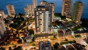 Ein Hochhaus-Hotel mit mehreren Stockwerken, umgeben von anderen Gebäuden und Blick auf das Meer.