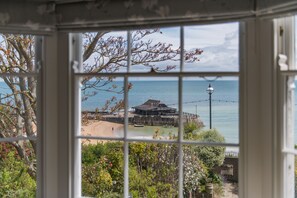 En vy genom ett fönster som visar ett kustnära område med en byggnad, en strand och havet.