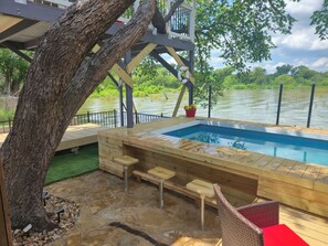 Una terraza de madera con piscina, suelo de piedra y un árbol.