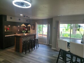 Una cocina moderna con barra, suelo de madera y ventanas amplias con vistas a zonas verdes.