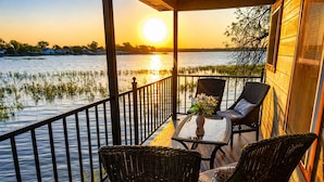 Een balkon met rieten meubilair en een glazen tafel, uitkijkend op het water bij zonsondergang.