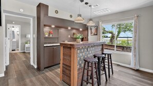 Een moderne keuken met een bar, houten vloeren, hanglampen en uitzicht op het buitengebied.