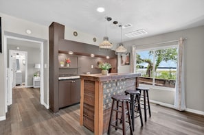Cocina moderna con barra, suelo de madera, iluminación colgante y vistas al exterior.