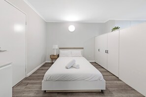 Ein modernes Hotelzimmer mit einem großen Bett, einem Nachttisch mit Lampe und einem Kleiderschrank.
